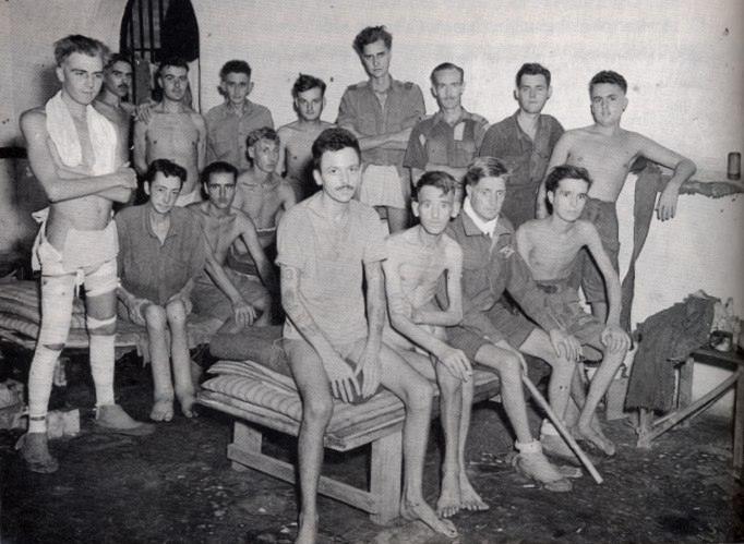 A group of emaciated prisoners, many bare-chested, posed together inside a cell block.