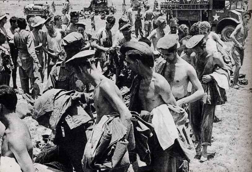 Freed prisoners sorting through piles of fresh clothing and kit beside army lorries.