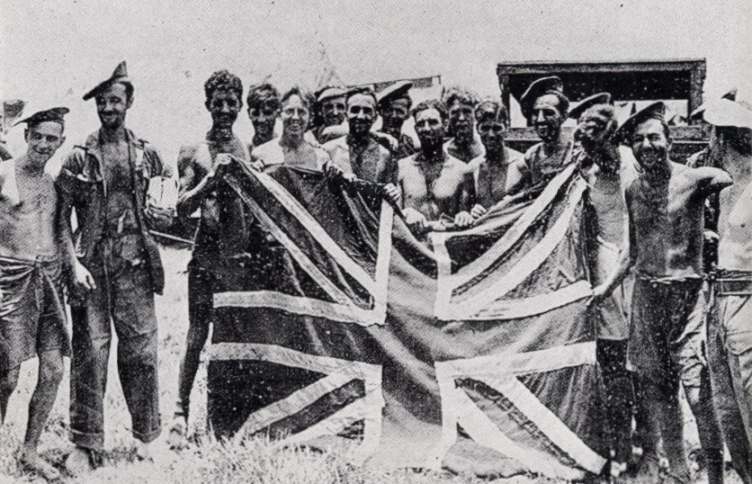 A line of smiling, thin former prisoners holding up a Union flag between them.