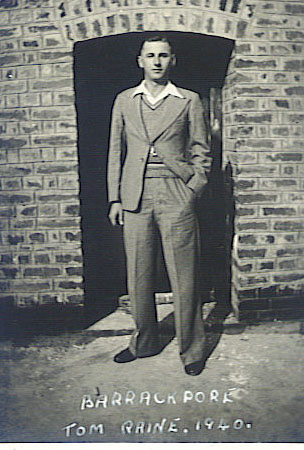 A young man in a suit standing before a brick archway; a caption on the photograph reads Barrackpore, Tom Raine, 1940.