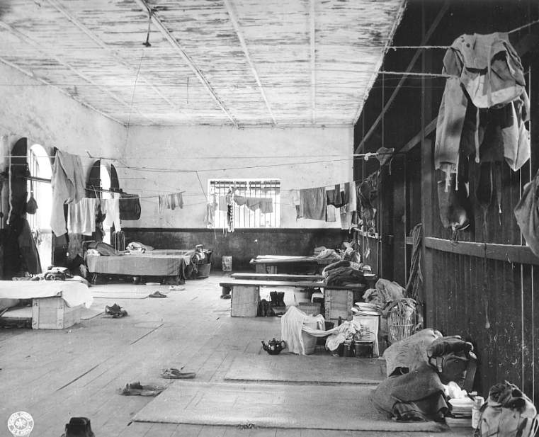 The interior of a prison dormitory with barred windows, low platforms and washing strung on lines.