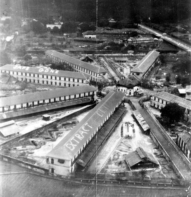An aerial photograph of Rangoon Jail, its long cell blocks radiating from a central hub, with large letters painted on the roofs.